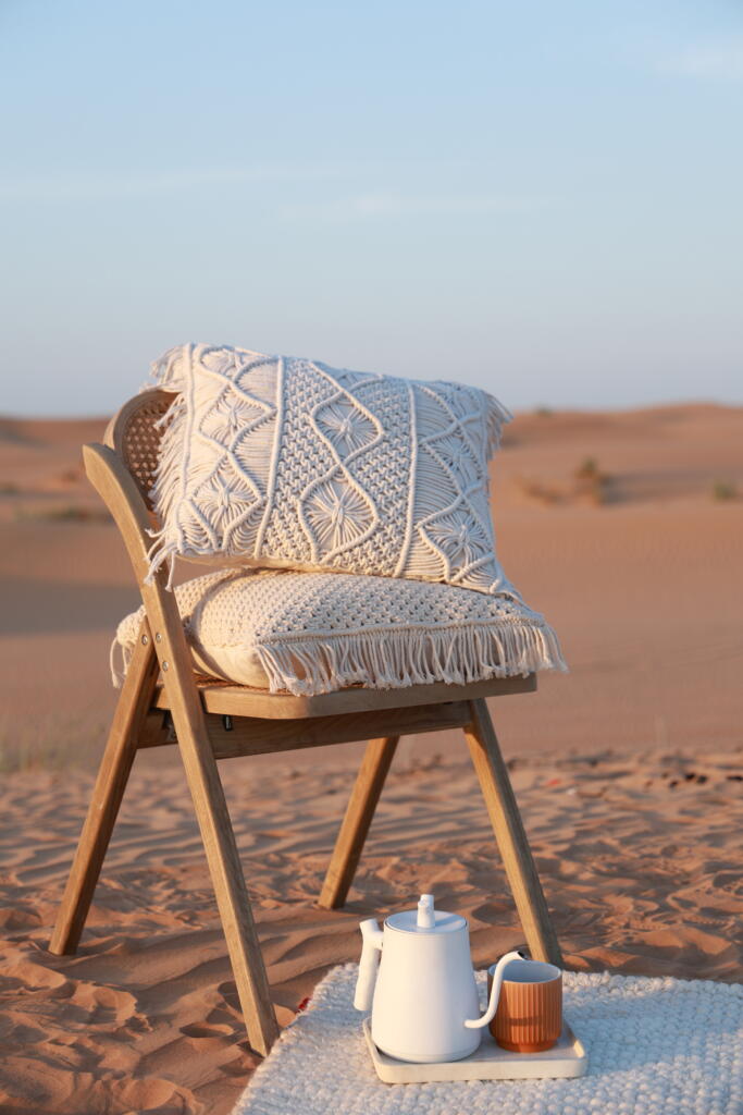 Handwoven cushion placed on a wooden chair in a desert setting with a teapot and cup on a mat